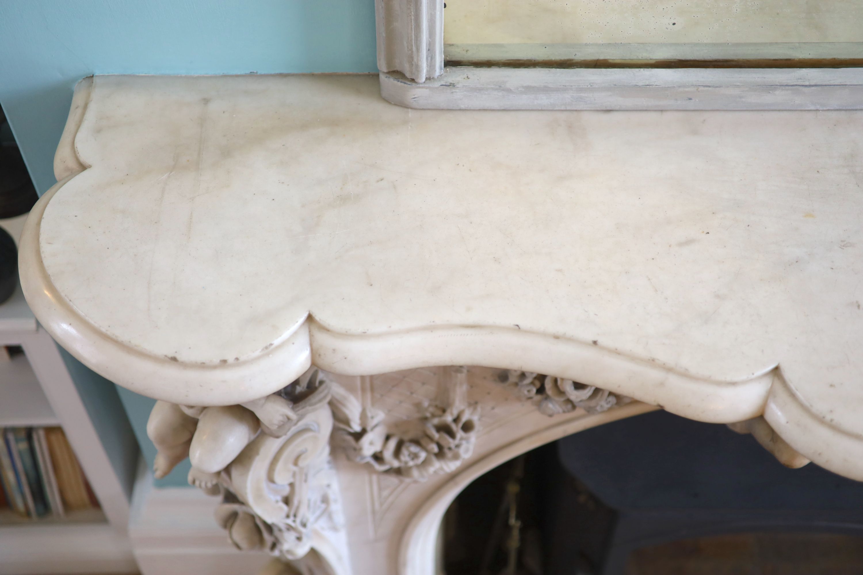 An important mid 19th century Italian white Carrara marble chimney piece, carved in the rococo taste, with seated putti, foliage swags